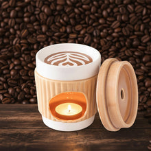Load image into Gallery viewer, white ceramic wax warmer with a lit candle inside, set against a coffee shop background.