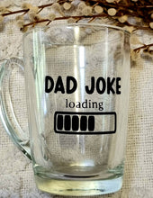 Load image into Gallery viewer, A clear glass mug with 'DAD JOKE LOADING' printed in black text, placed on a textured surface with a dry branch in the background.