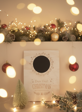 Load image into Gallery viewer, A wooden countdown board with a chalkboard vinyl surface, featuring text 'Days until Christmas' and a circular black area to mark the days, accompanied by a wooden easel stand and a green Christmas tree with lights in the background.