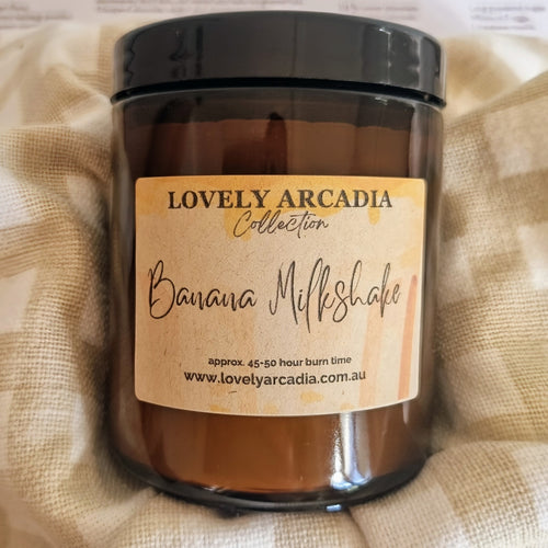 Candle jar with 'Lovely Arcadia' label on a textured fabric background. Banana Milkshake 