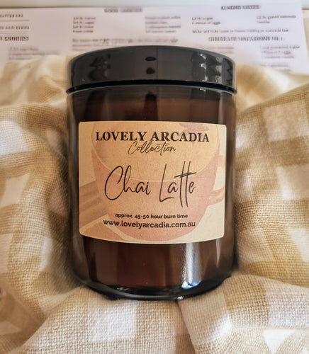 Candle with 'Lovely Arcadia' label on a textured fabric background. Chai Latte