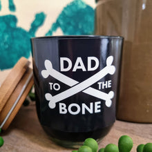Load image into Gallery viewer, Black soy wax candle in a glass jar with a lid, featuring white text &#39;DAD TO THE BONE&#39; and bone graphics on the front.
