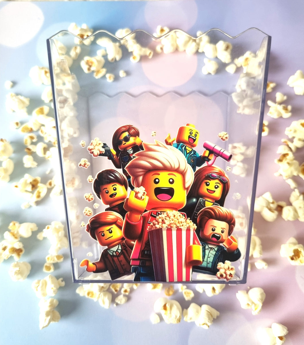 Transparent acrylic standee with cartoon characters and popcorn, surrounded by real popcorn on a light blue background.