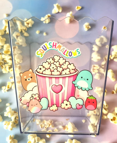 Clear container with Squishmallows design featuring a popcorn bucket and cute characters, surrounded by popcorn.