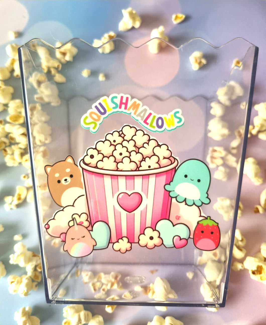 Clear container with Squishmallows design featuring a popcorn bucket and cute characters, surrounded by popcorn.