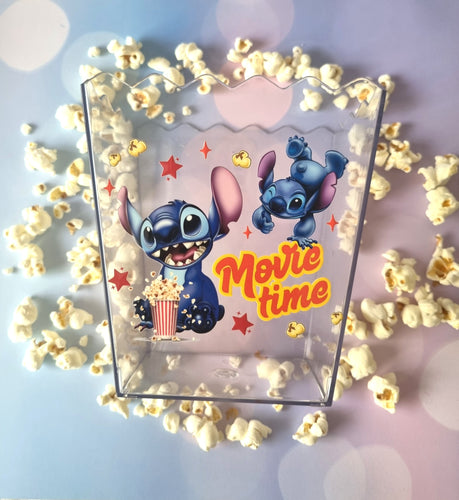 Clear popcorn bucket with cartoon characters and 'Movie time' text, surrounded by popcorn on a light blue background.