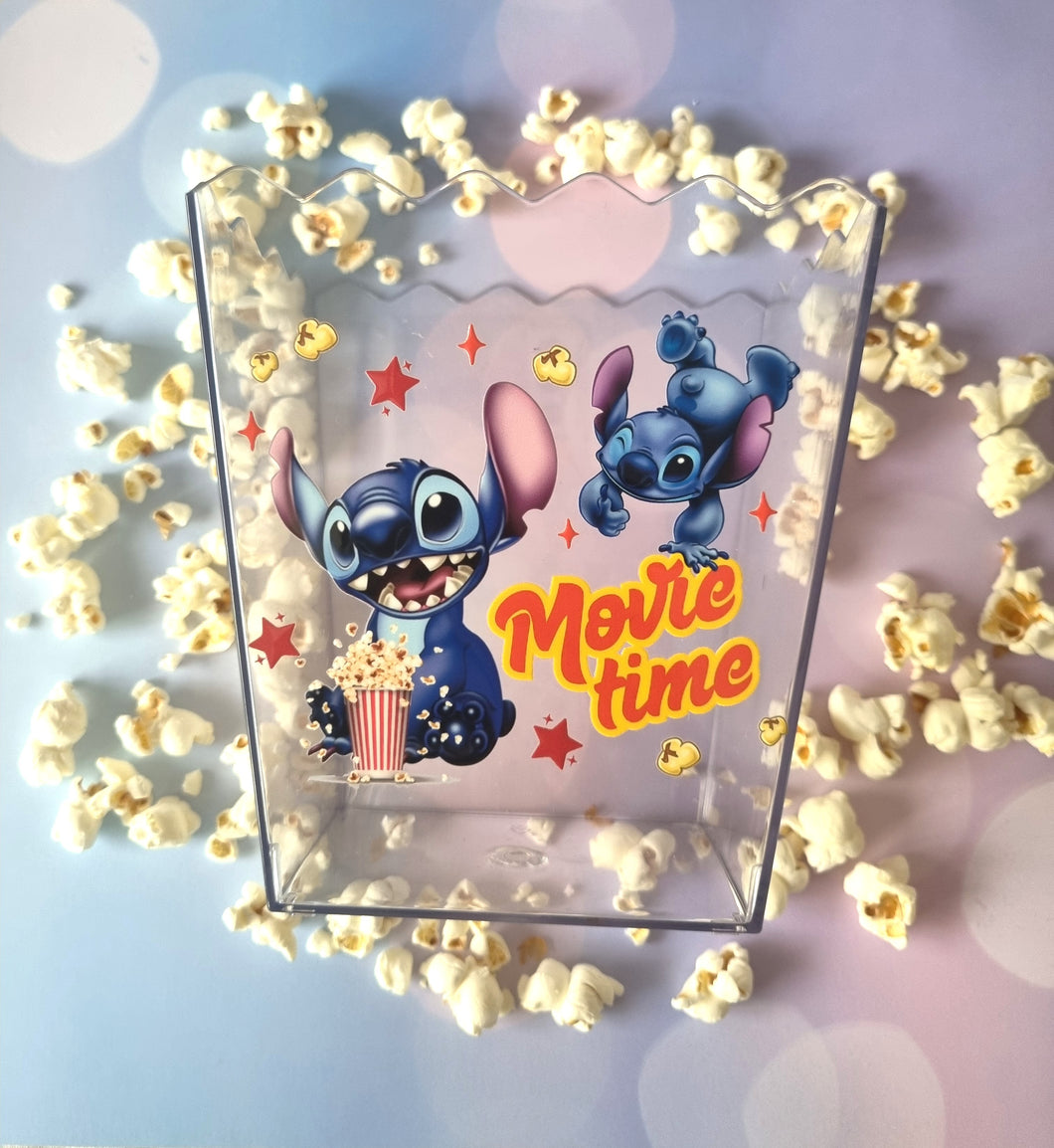 Clear popcorn bucket with cartoon characters and 'Movie time' text, surrounded by popcorn on a light blue background.