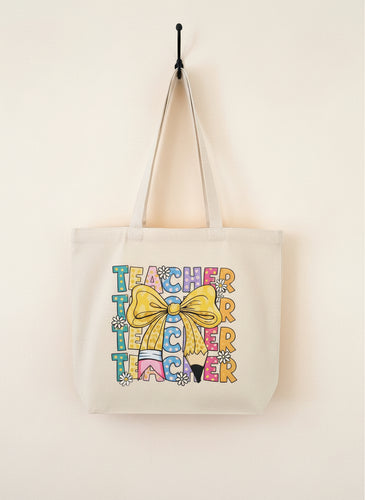 Beige tote bag with colorful 'Teacher' text and a yellow bow on a wooden surface.