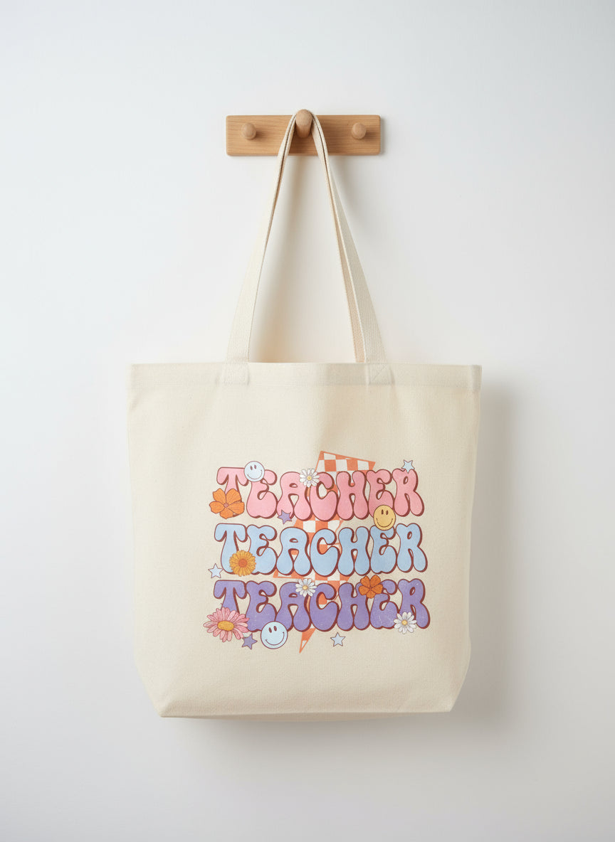 Beige tote bag with colorful 'Teacher Teacher Teacher' text and decorative elements on a beige background.