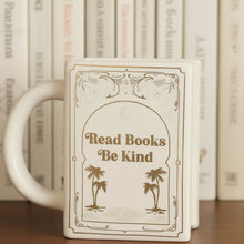 Load image into Gallery viewer, White mug with decorative text and palm tree design, placed on a surface with a book in the background.
